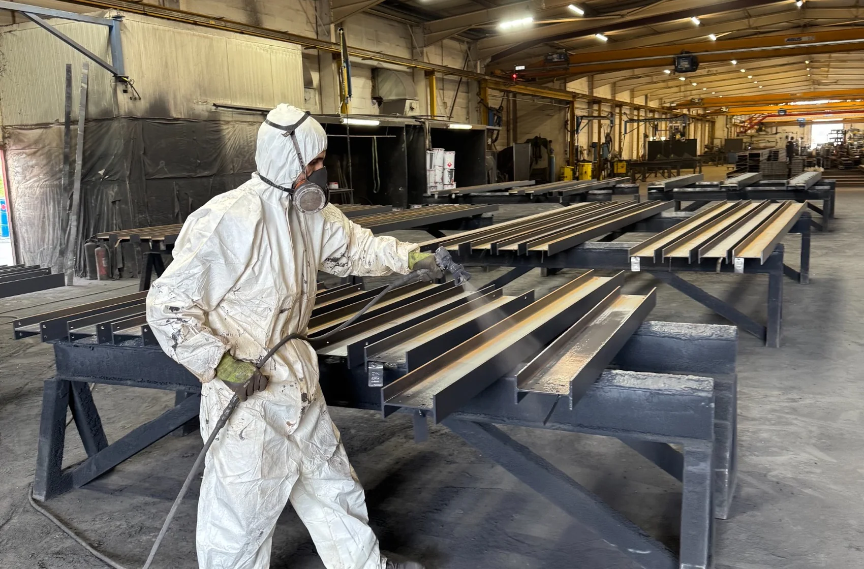 Applicateur peinture industriel en combinaison travaillant sur des éléments métalliques